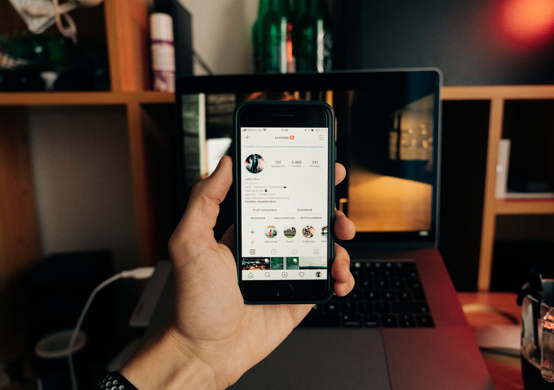Perfil de rede social aberto no celular ao lado de um notebook em um escritório